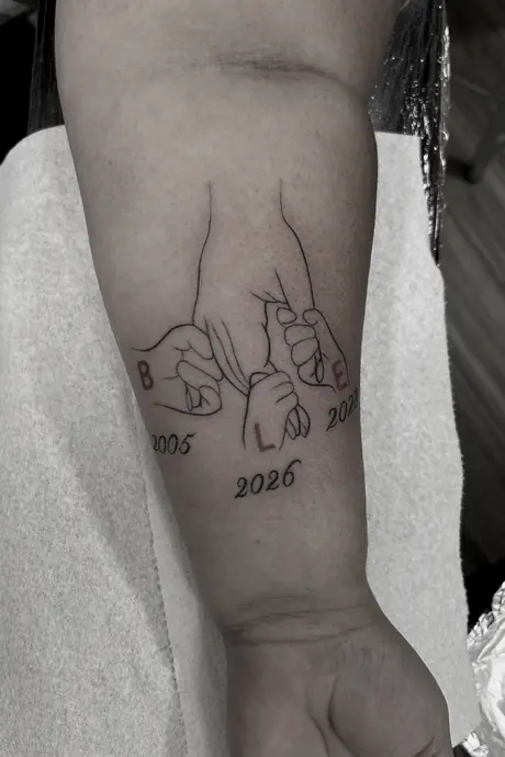 Fine line memorial forearm piece of two hands making a pinky promise, with names and dates picked out in red.