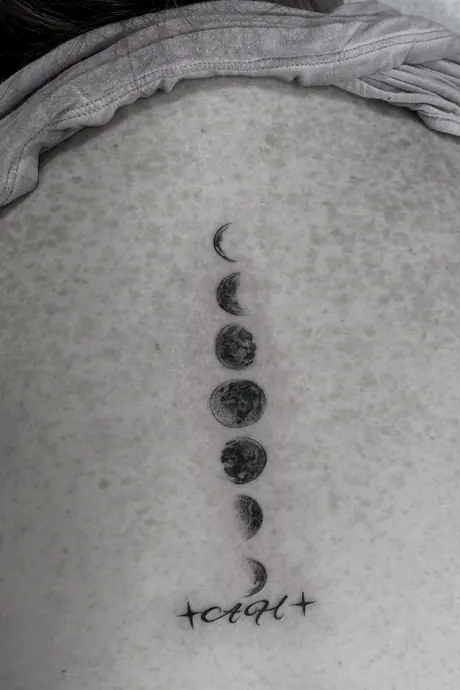 Fine line moon phases running down a spine with a short line of script beneath them.