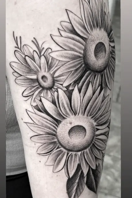 Black and grey sunflower cluster on a forearm, softly shaded with stippled centers.