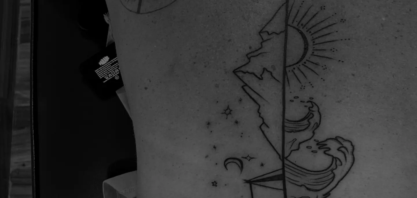 A fine line tree and sun tattoo running down a client's spine, worked in black and grey.
